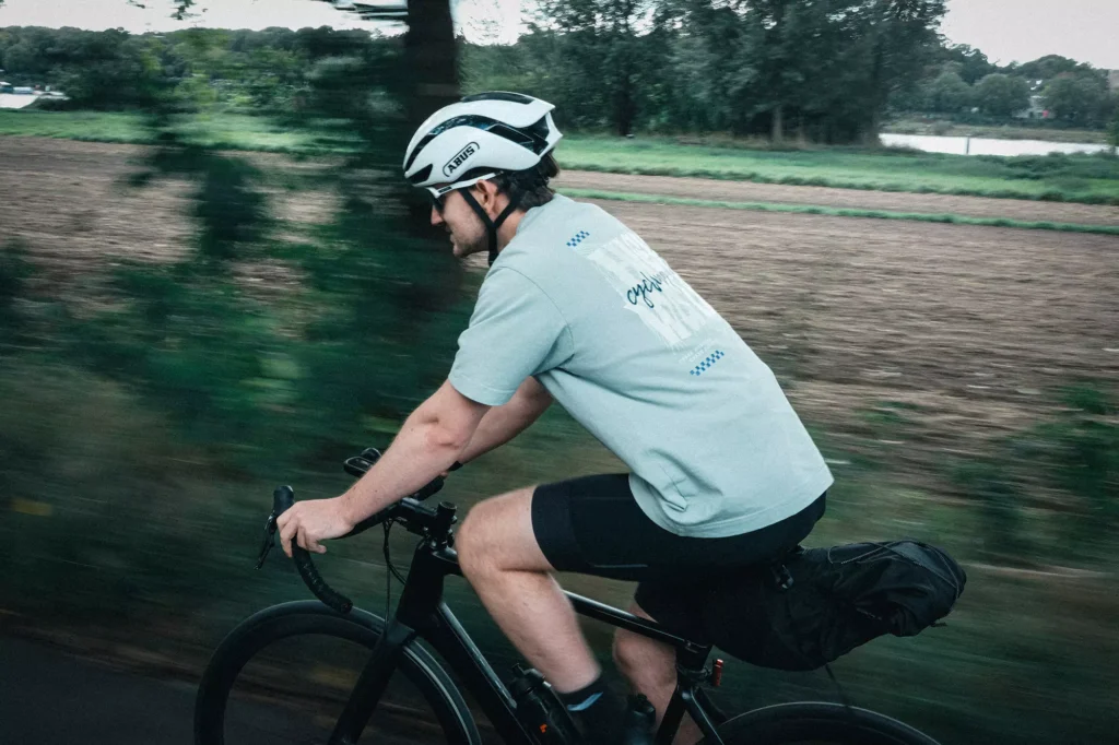 A man riding his bicycle next to a field wearing a Cypha Cycling T-Shirt